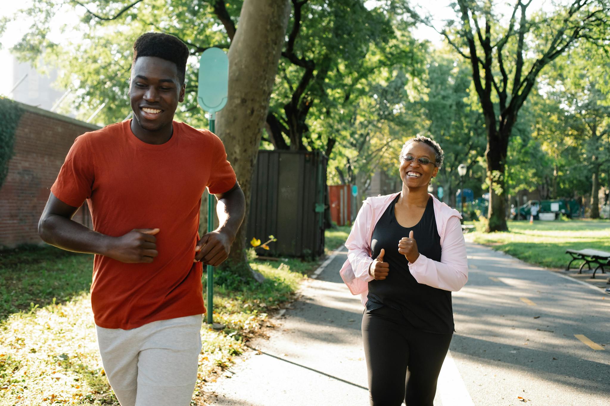 A smiling couple jogging together in a sunny park setting.