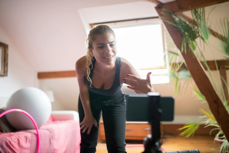 A woman energetically leads a virtual fitness class from her home, engaging with her audience online.